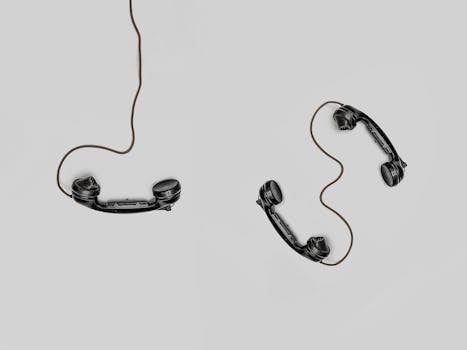 Contact Two vintage black telephone handsets connected by cords on gray background.